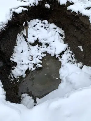 Open excavation with snow along the ground and exposed pipework.