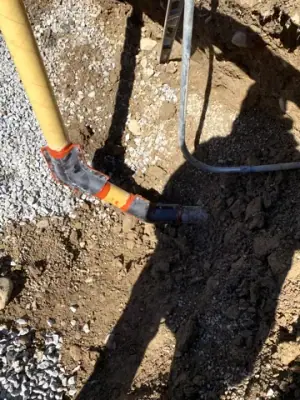 Underground pipe and conduit connections exposed beside the trench wall.