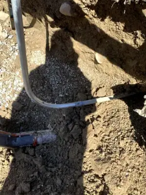 Underground pipe and conduit connections exposed beside the trench wall.