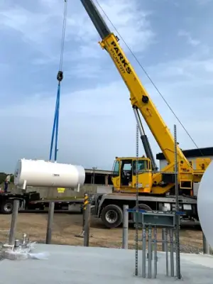 Crane lifting equipment positioned beside the tank and concrete foundation.