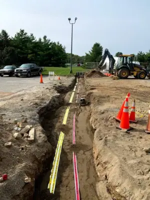 Utility trench with warning tape and partially covered service runs.