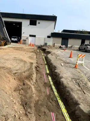 Utility trench with warning tape and partially covered service runs.