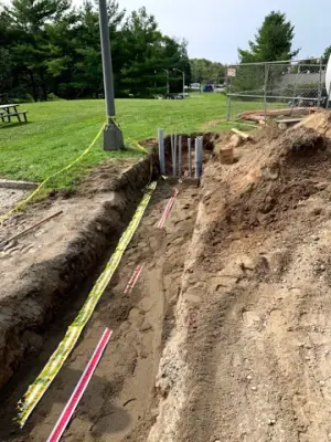 Utility trench with warning tape and partially covered service runs.