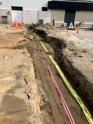 Utility trench with warning tape and partially covered service runs.