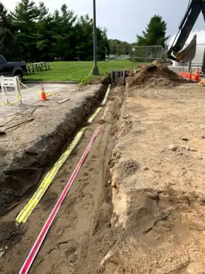 Utility trench with warning tape and partially covered service runs.