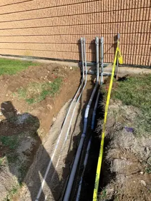 Service lines rise from the trench beside the building wall.