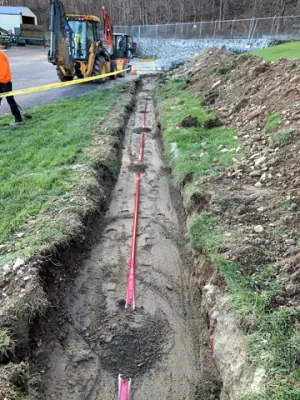 Partially backfilled utility trench with red warning tape.