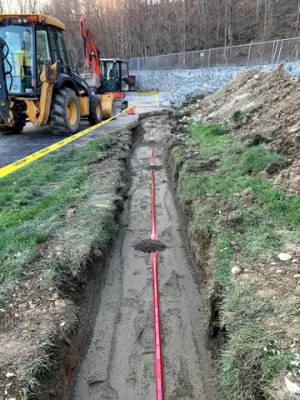 Partially backfilled utility trench with red warning tape.