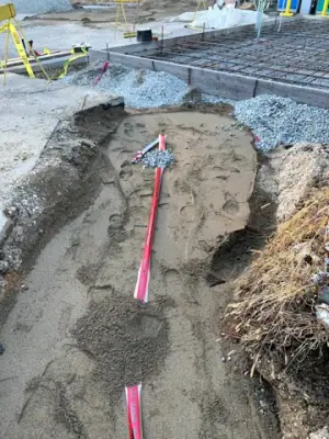 Partially backfilled utility trench with red warning tape.