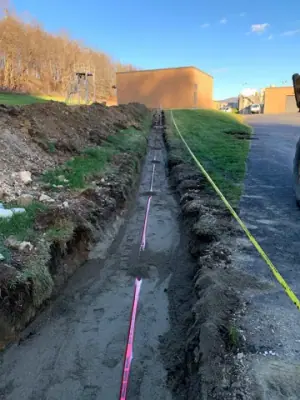 Partially backfilled utility trench with red warning tape.