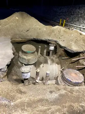 Excavation exposes tank-top access points and buried equipment.