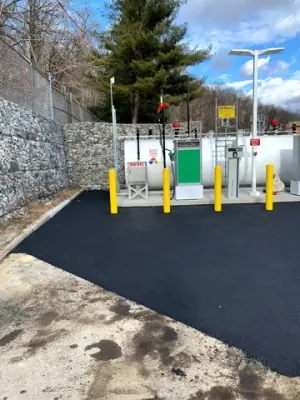 Fresh asphalt around the installed fueling equipment and protective bollards.
