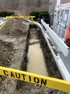 Open trench beside the building, cordoned off with caution tape.