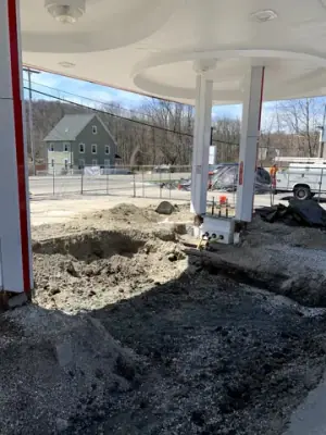Excavated fueling-island area with open channels and earthmoving equipment.