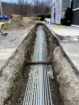 Parallel electrical conduits laid in an open trench beneath the forecourt.
