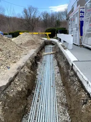 Parallel electrical conduits laid in an open trench beneath the forecourt.