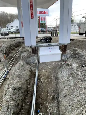 Underground lines run through a narrow excavation toward a canopy column.