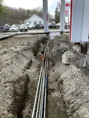 Underground lines run through a narrow excavation toward a canopy column.