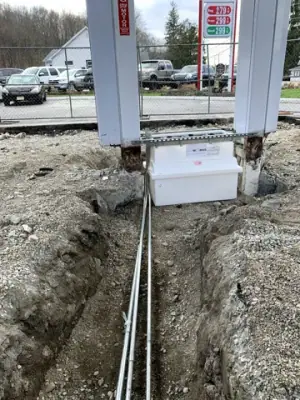 Underground lines run through a narrow excavation toward a canopy column.
