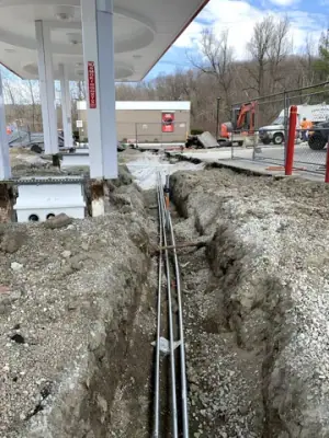 Underground lines run through a narrow excavation toward a canopy column.