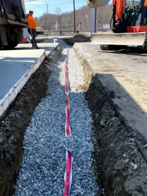 Gravel backfill and red warning tape along the utility trench.
