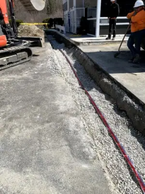 Gravel backfill and red warning tape along the utility trench.