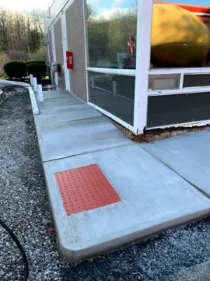 Concrete walkway with a red tactile warning panel at the corner.