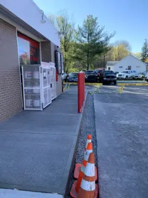 Finished sidewalk along the building with protective red posts.