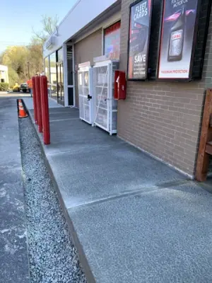 Finished sidewalk along the building with protective red posts.