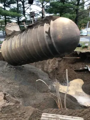 Cylindrical tank suspended above the excavation during lifting.
