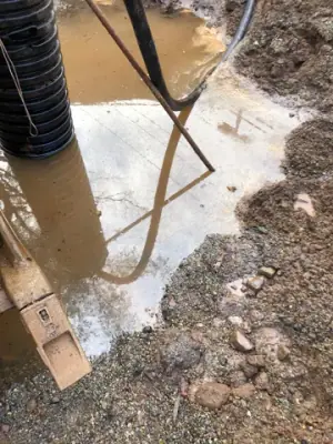 Hoses and a vertical pipe in water at the bottom of the excavation.
