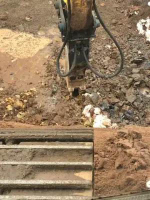 Excavator-mounted breaker working on rock in the excavation.