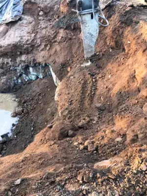 Earth walls, exposed lines, and water in the tank excavation.