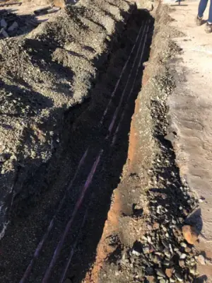 Narrow trench with exposed underground lines.