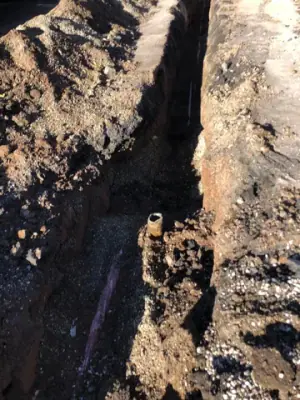 Narrow trench with exposed underground lines.
