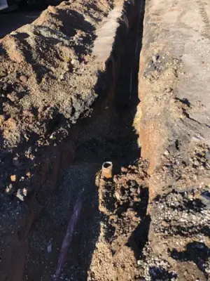Narrow trench with exposed underground lines.
