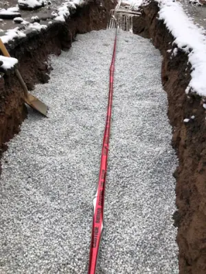 Aggregate backfill with red warning tape along the trench.