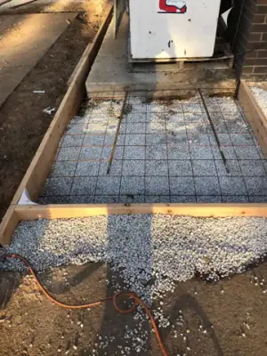 Narrow concrete form with reinforcing mesh beside a dispenser base.