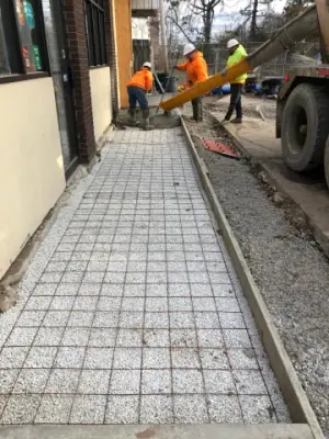 Crew placing concrete along the building-side walkway.