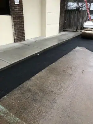 New asphalt strip meets the raised concrete walkway.