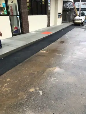 Asphalt strip runs along the finished storefront walkway.