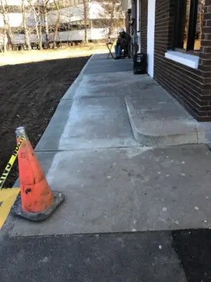 Concrete walkway along the building, marked with a traffic cone.